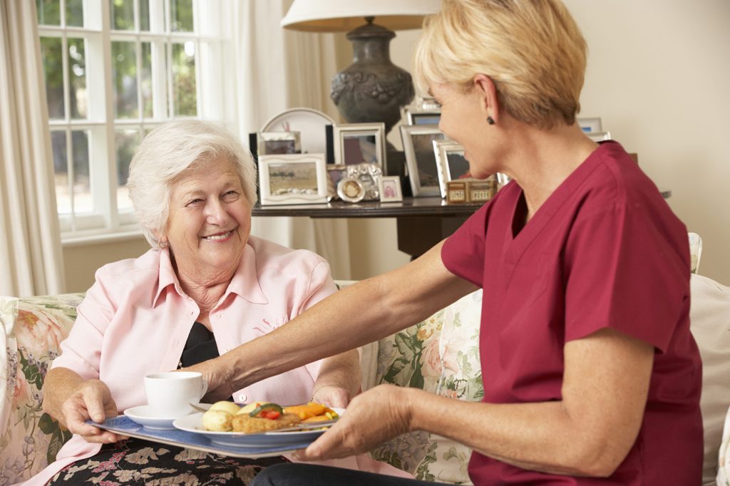 Die fürsorgliche Pflegerin gibt der Seniorin einen Teller mit Essen und lächelt